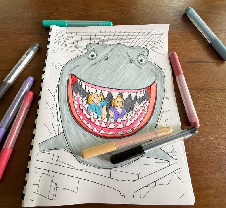 Printed coloring book with a shark design and markers on a table